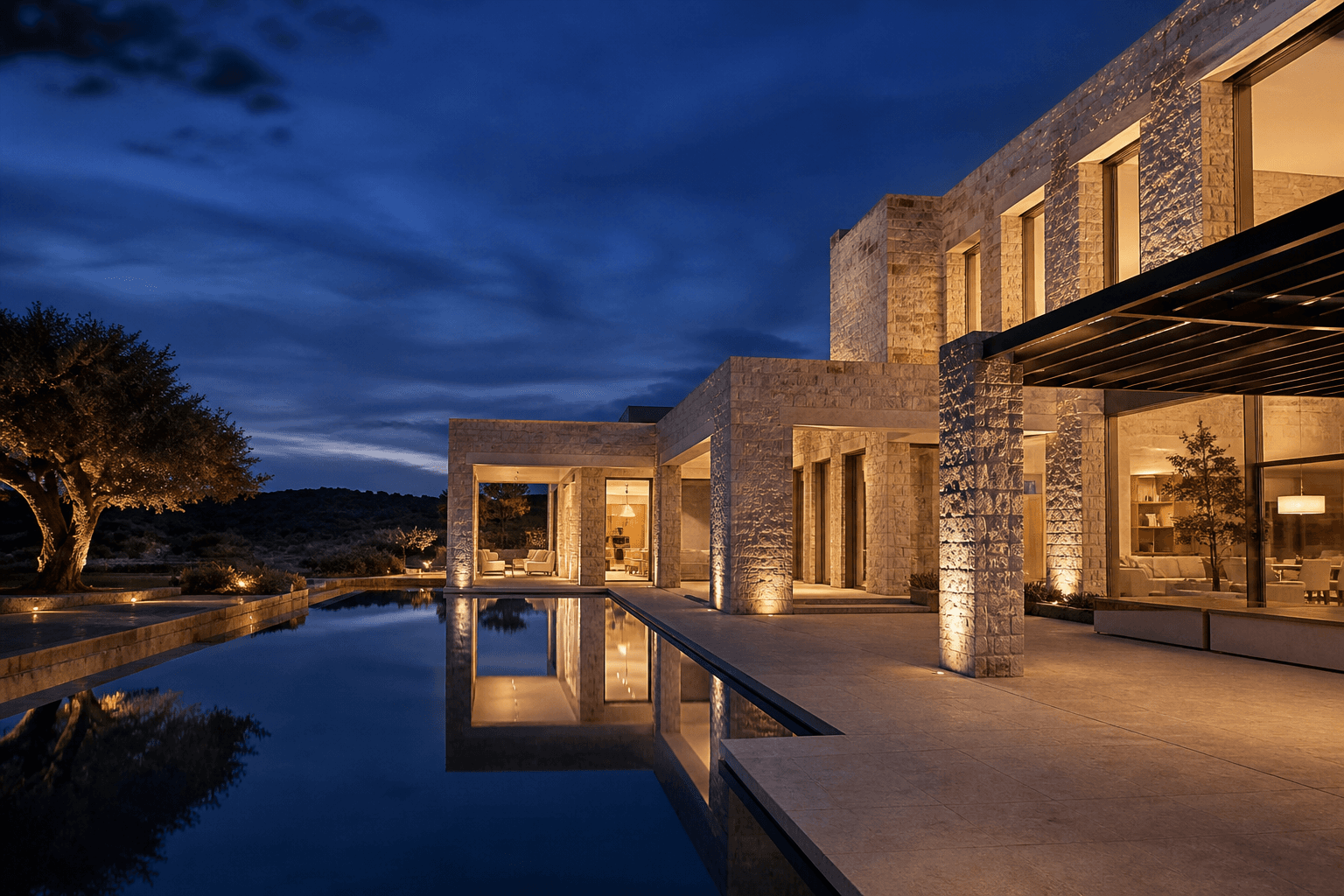 A contemporary residence at blue hour: still pool, limestone, and warm light behind glass.